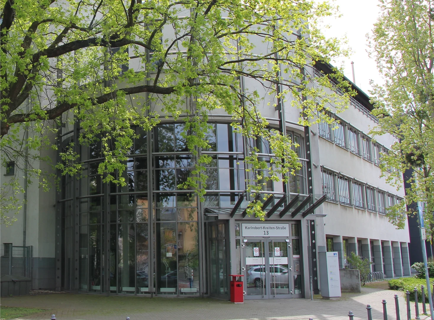 Eine Wissenschaftlerin und ein Wissenschaftler arbeiten hinter einer Glasfassade und mischen Chemikalien mit Großgeräten.